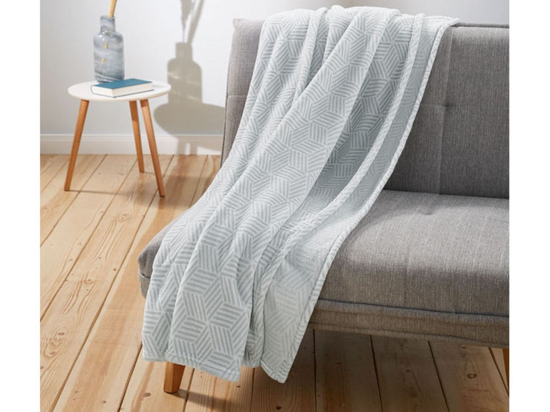 Eine graue Decke mit geometrischem Muster auf einem grauen Sofa.