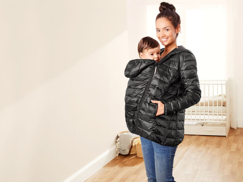 Eine Frau trägt eine schwarze Jacke mit einem Baby in einer Tragehilfe