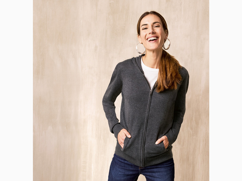 Eine Frau trägt einen grauen Hoodie und blaue Jeans.