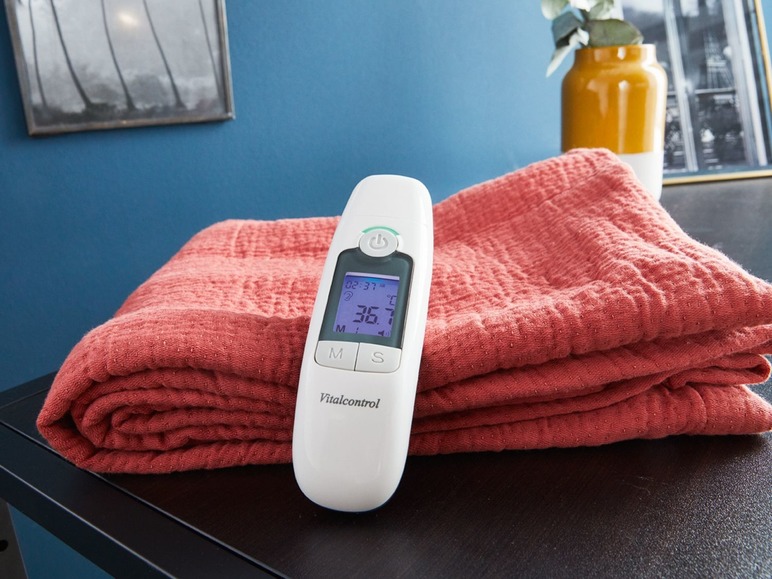 Ein Vitalcontrol Thermometer auf einer roten Decke.