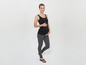 Eine schwangere Frau in einem schwarzen Tanktop und grauen Leggings.