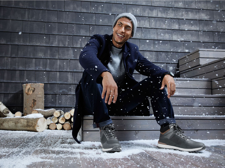 Mann in Winterjacke und Stiefeln sitzt auf einer Holztreppe im Schnee.