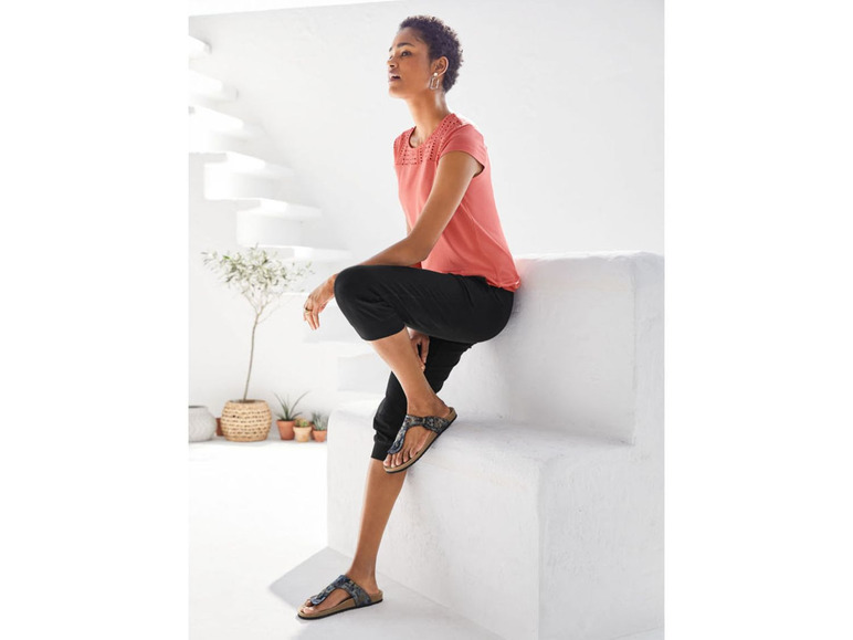 Frau in einem rosafarbenen Shirt, schwarzen Hosen und Birkenstock-Sandalen.