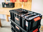 Stapelbare schwarze Aufbewahrungsboxen mit roten Griffen, Marke Qbrick System.