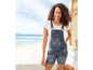 Eine Frau trägt eine Denim-Overall-Shorts am Strand.