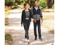 Ein Mann und eine Frau tragen schwarze Jogginghosen und Kapuzenpullover beim Spaziergang.