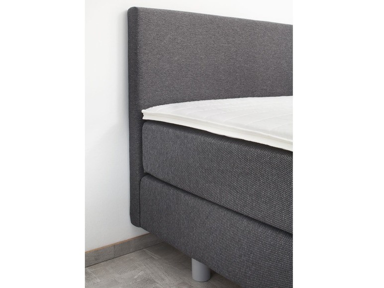 Ein graues Boxspringbett mit weißem Topper.