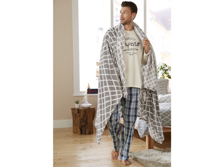 Mann mit einer grauen Decke und blauen karierten Schlafanzug-Hosen.
