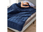 Eine blaue Gewichtsdecke auf einem Bett, mit einer Person, die darunter schläft.