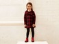Ein Mädchen trägt ein rot-schwarzes kariertes Kleid, schwarze Leggings und rote Stiefel.