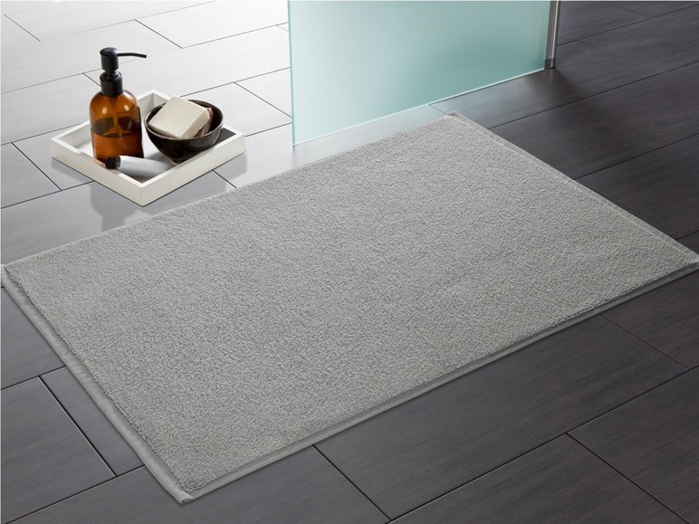 Ein grauer Badezimmerteppich in einem Badezimmer mit einem Spender und einem Stück Seife.