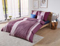 Ein rosafarbenes und violettes Bettbezug mit geometrischem Muster auf einem Bett.