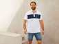 Ein Mann trägt ein weißes Poloshirt mit blauen Details und blaue Denimshorts.