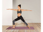 Eine Frau in Sport-BH und Leggings macht Yoga auf einer lila Matte.