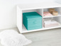 Eine türkisfarbene Aufbewahrungsbox auf einem weißen Regal mit einem weißen Teppich.