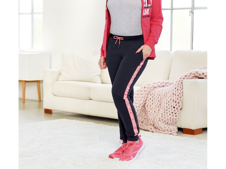 Eine Frau in schwarzen Jogginghosen mit rosa Hoodie und rosafarbenen Sneakers.