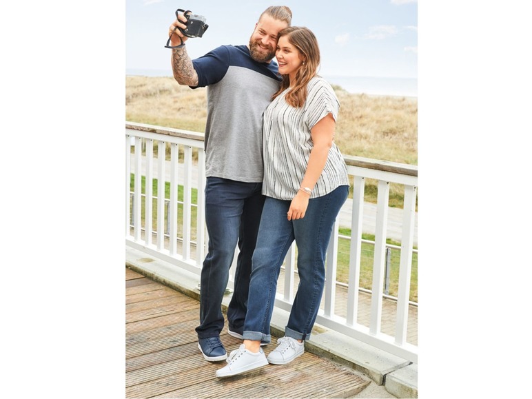 Ein Paar posiert in Jeans und T-Shirts auf einem Holzsteg.