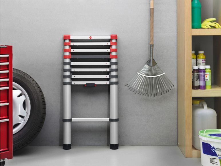 Eine Teleskopleiter in einer Garage mit einem Werkzeugschrank, einem Rad, einer Harke und anderen Werkzeugen.