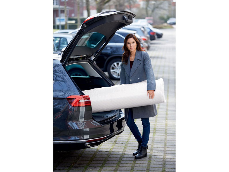Eine Frau lädt eine Matratze in den Kofferraum eines Autos.