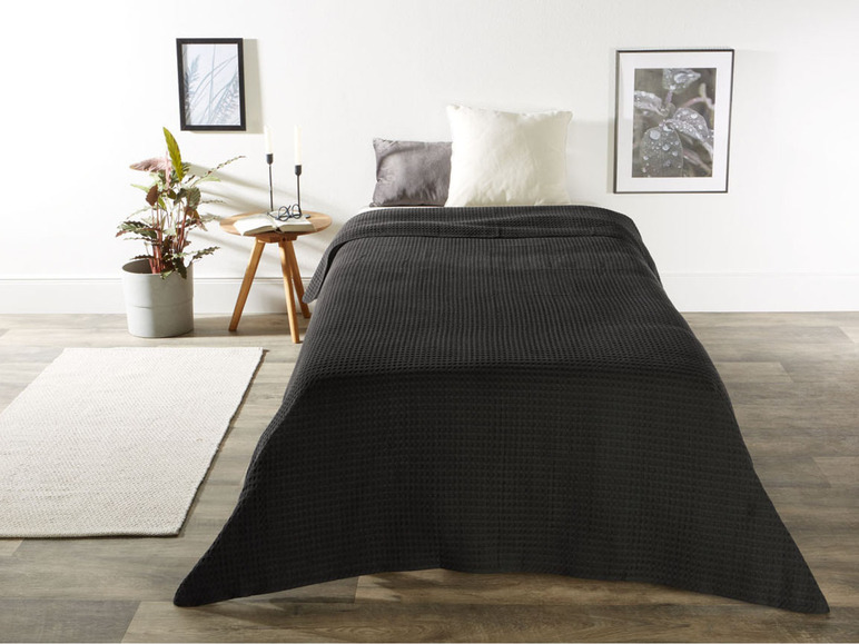 Eine dunkelgraue Frotteedecke auf einem Bett mit Kissen.