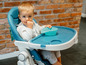 Ein Baby sitzt in einem blauen Hochstuhl mit einer blauen Schüssel.