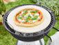 Eine Pizza auf einem Pizzastein auf einem schwarzen Grill.