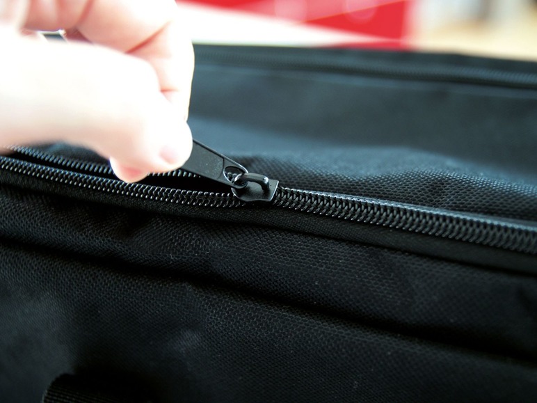 Eine Hand öffnet einen schwarzen Reißverschluss an einer Tasche.