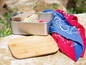 Ein Sandwich in einer Metall-Lunchbox mit einem Holzbrett und einem Bandana