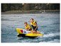 Zwei Jungen auf einem gelben Schlauchboot mit dem Schriftzug 'Sinner' werden durchs Wasser gezogen.