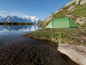 Ein grünes Zelt am Ufer eines Sees vor einer Bergkulisse.