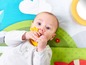 Ein Baby spielt mit einem gelben Beißring auf einer Spielmatte.