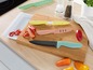 Ein Set mit farbigen Messern auf einem Holzbrett mit Paprika.