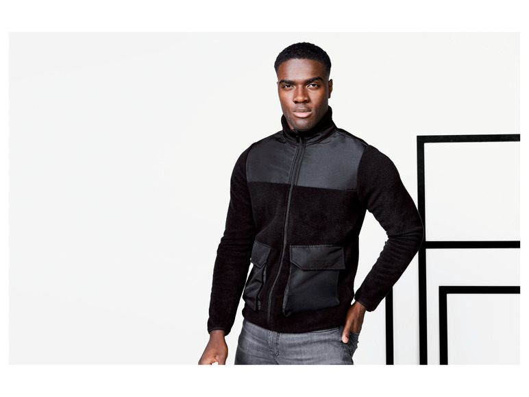 Ein Mann trägt eine schwarze Fleecejacke mit großer Tasche.