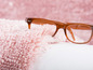 Eine braune Brille auf einem rosafarbenen flauschigen Teppich.