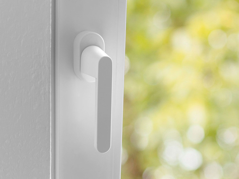 Ein weißer Fenstergriff vor einem verschwommenen grünen Hintergrund.