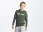 Ein Junge trägt einen grünen Pullover mit 'New York' Aufdruck und graue Hose.