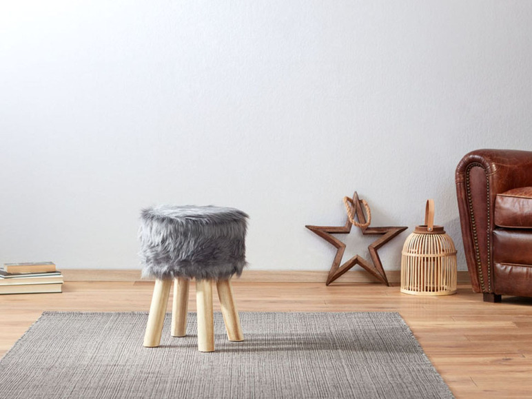 Ein grauer Fellhocker mit Holzbeinen auf einem Teppich.