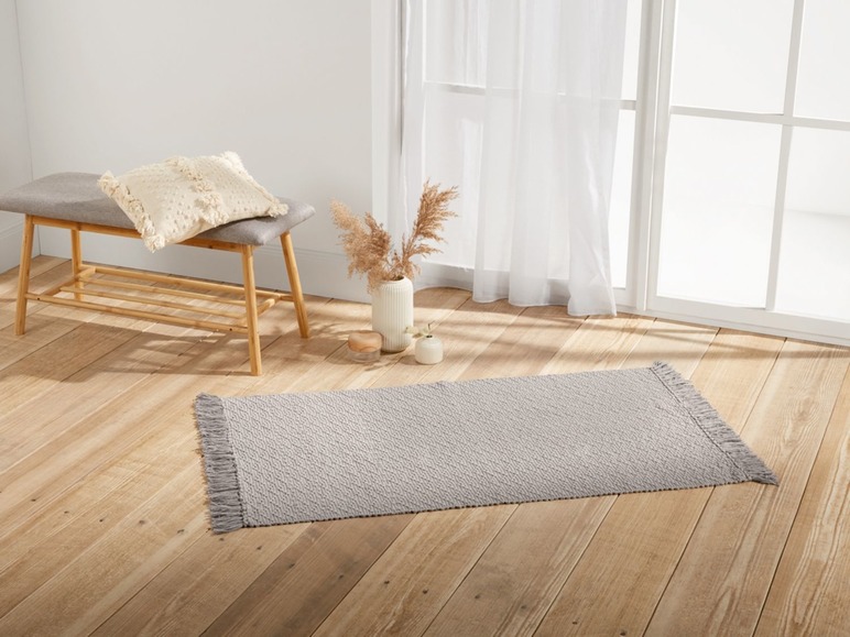 Ein grauer Teppich mit Fransen auf einem Holzboden.