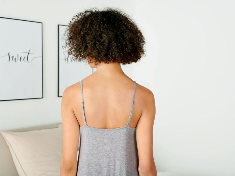 Frau in einem grauen Kleid steht in einem Schlafzimmer.