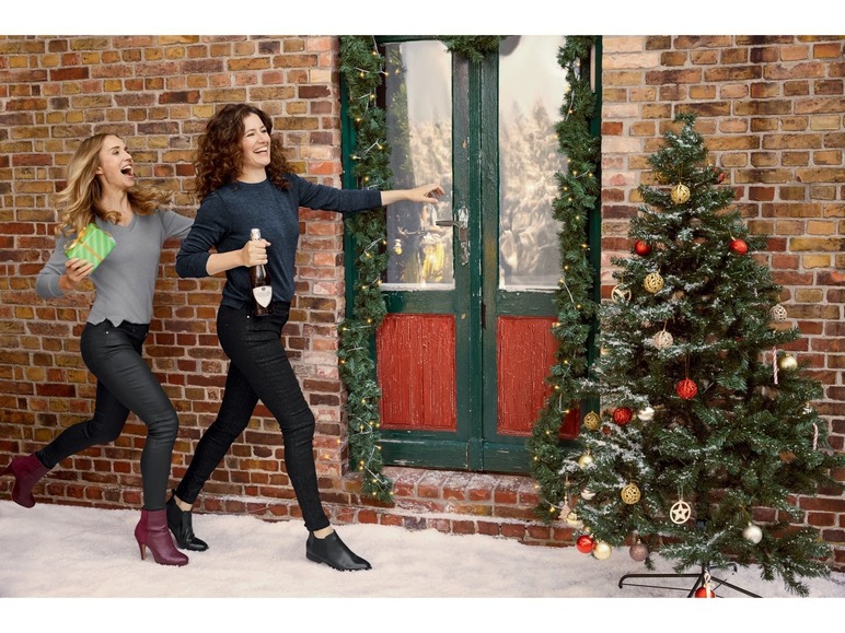 Zwei Frauen gehen mit Geschenken und Champagner zu einem Weihnachtsbaum.
