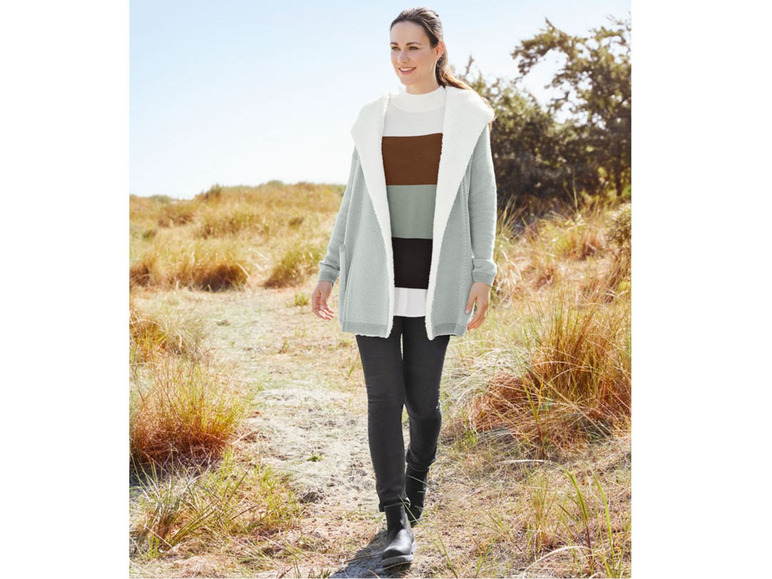 Eine Frau trägt eine graue Kapuzenjacke mit einem gestreiften Pullover darunter.