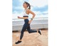 Eine Frau läuft in Sport-BH und Leggings mit einer Smartwatch.