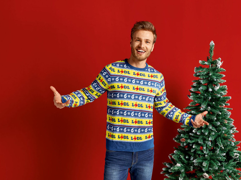 Mann in einem Lidl-Weihnachtspullover neben einem Weihnachtsbaum.