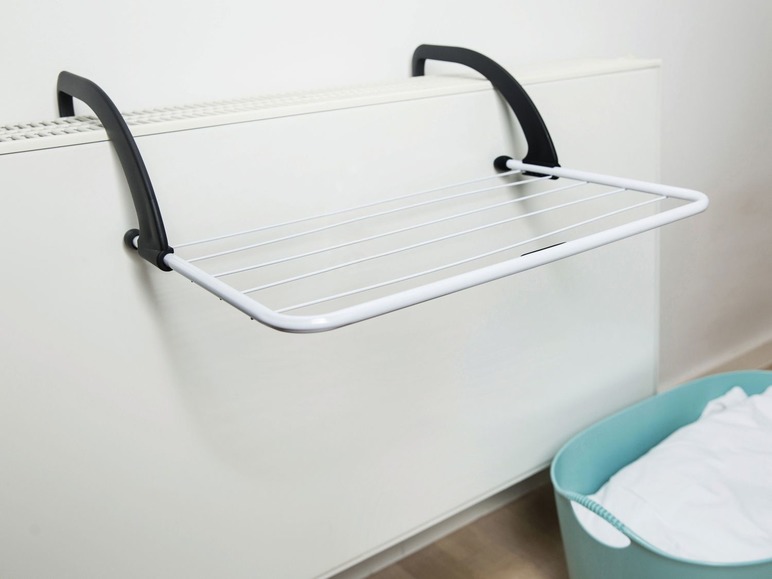 Ein weißer Wäschetrockner mit schwarzen Halterungen, an einem Heizkörper befestigt.