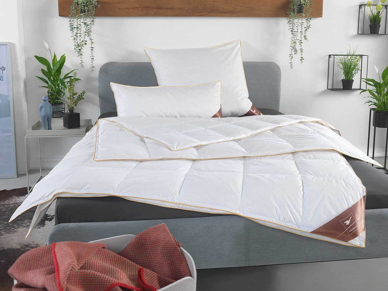 Eine weiße Bettdecke mit goldenen Rand, auf einem Bett mit Kissen