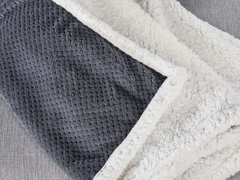 Eine graue und weiße Fleecedecke mit einem Gittermuster.