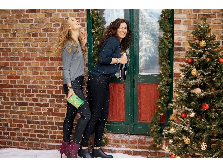 Zwei Frauen mit Weihnachtsgeschenken und Champagner vor einer winterlichen Weihnachtsdekoration.