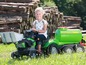 Ein Kind fährt einen grünen John Deere Traktor mit Anhänger.