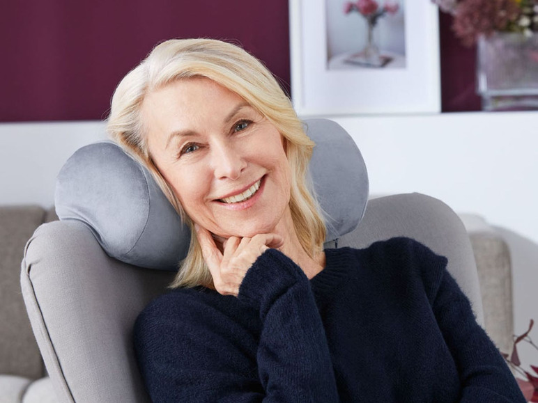 Eine Frau mit einem grauen Nackenstützkissen in einem Sessel.