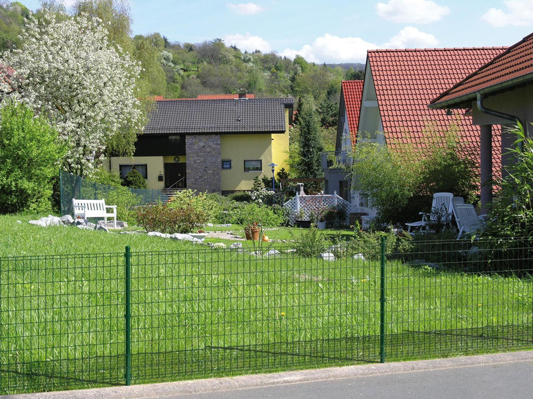 Ein grüner Zaun vor einem Haus mit rotem Dach